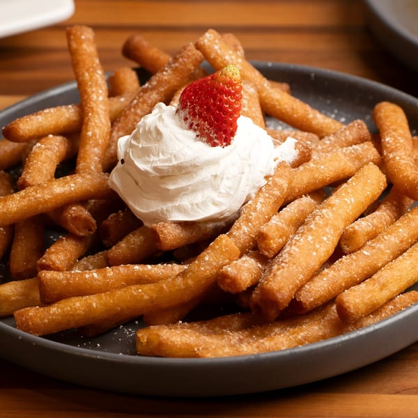 Golden churro fries dusted with powdered sugar, topped with whipped cream and a fresh strawberry.