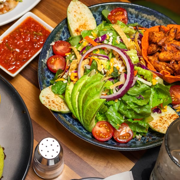 A vibrant salad with avocado, tomatoes, red onion, and chicken in a blue bowl.