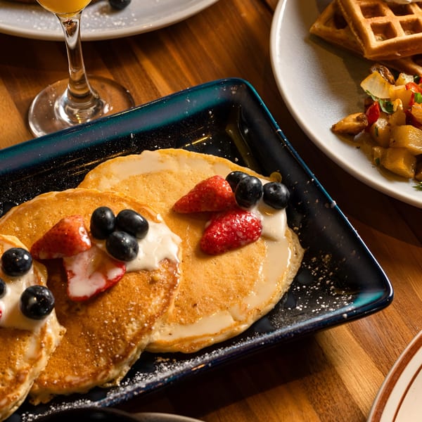 Pancakes topped with strawberries, blueberries, and cream, alongside waffles and potatoes.