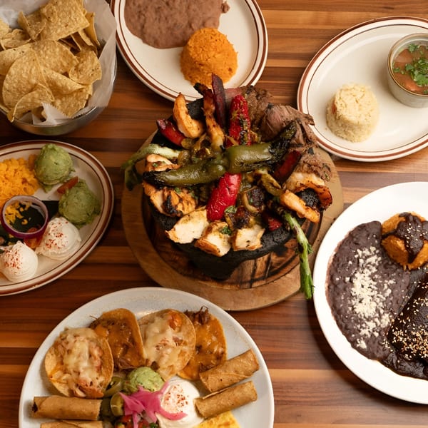 A table laden with various Tex-Mex dishes, including a large molcajete with grilled meats and vegetables.