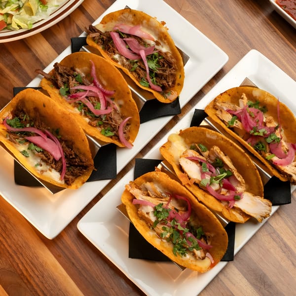 Two plates of tacos, one with beef and the other with chicken, topped with pickled onions and cilantro.