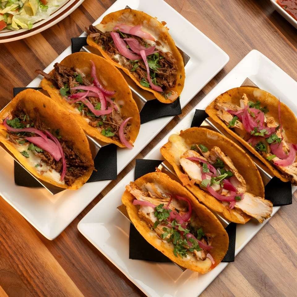 Two plates of tacos, one with beef and the other with chicken, topped with pickled onions and cilantro.
