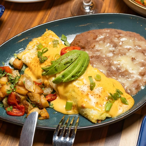 A breakfast plate with a cheese omelet topped with avocado, home fries, and refried beans.