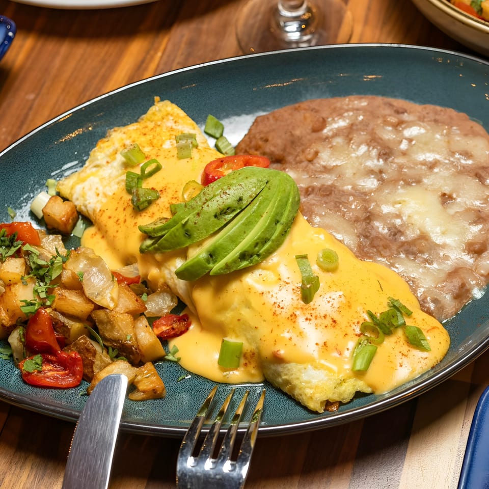 A breakfast plate with a cheese omelet topped with avocado, home fries, and refried beans.